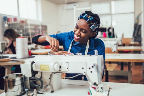 Young african textile worker sewing on production line. Dressmaker woman working with sewing machine